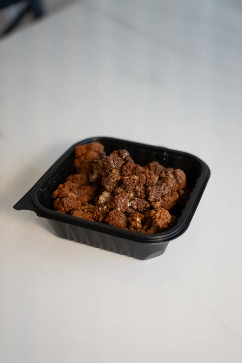 Crispy fried cauliflower in a to-go box on a marble counter