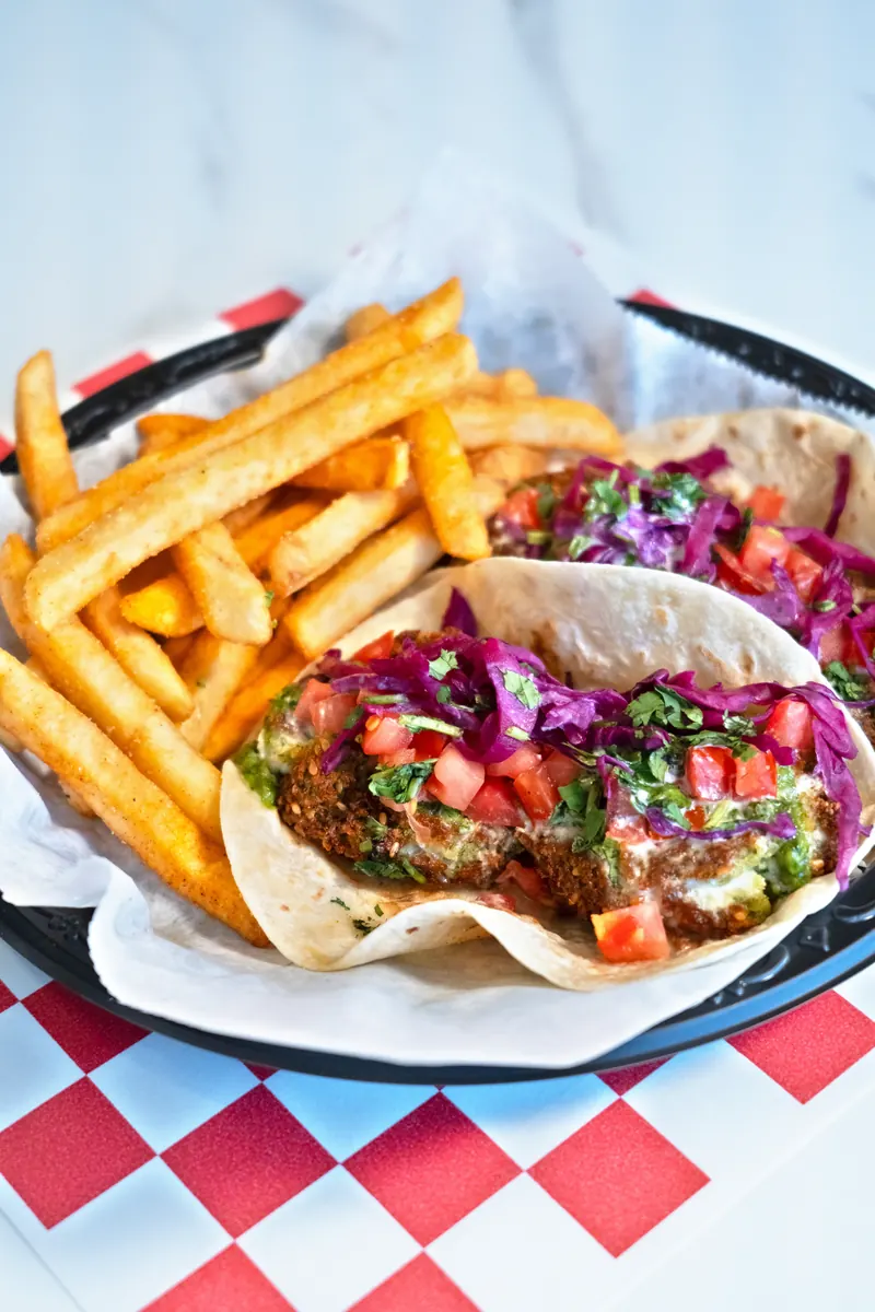 Two spicy falafel tacos and fries in a basket lined with checkered paper