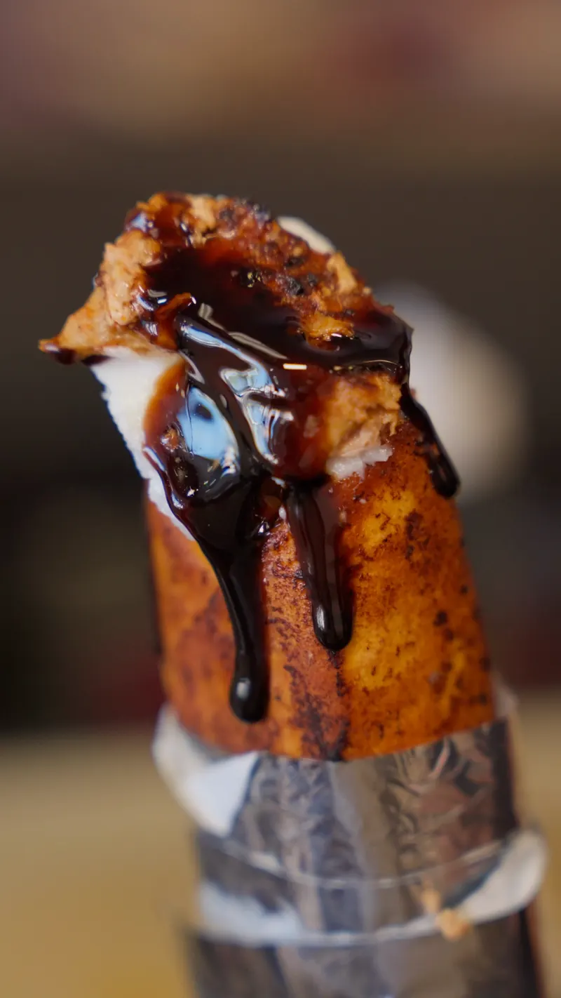 A crispy shawarma wrap standing in its foil, finished with a dark sauce drizzle