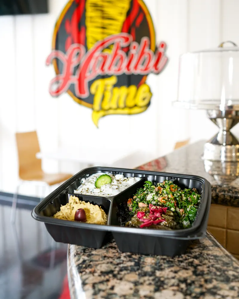 A combo box of hummus, rice and tabbouleh on the counter under the logo