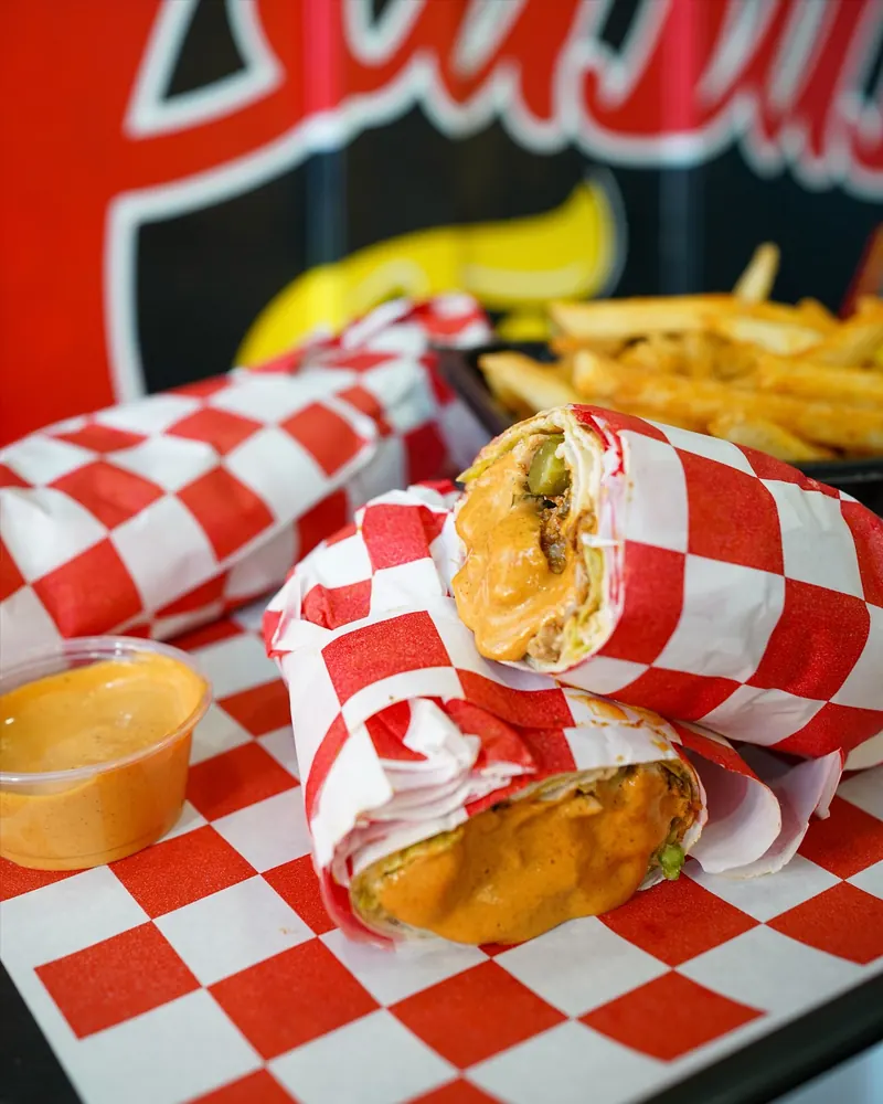 A crispy shawarma wrap in checkered paper with a cup of sauce