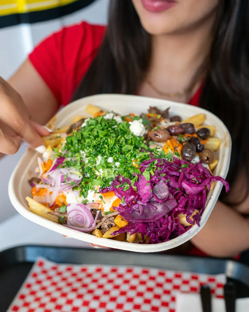 Holding a loaded fries bowl topped with parsley and pickled cabbage
