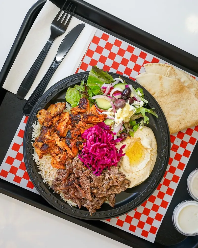 Mixed shawarma plate with rice, hummus, salad and pita on a checkered tray