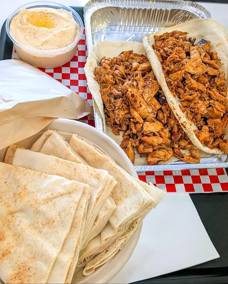 Chicken shawarma in pita with a side of hummus on checkered paper