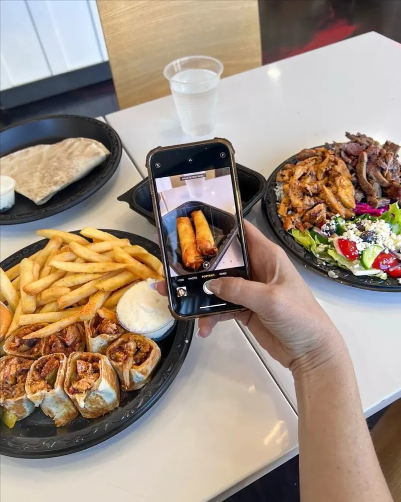 Taking a phone photo of shawarma bites and a plate at the table