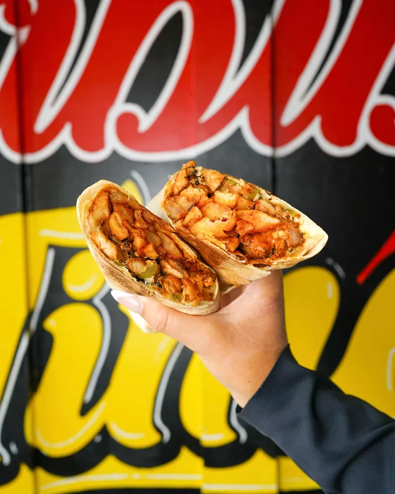 A chicken shawarma wrap held up in front of the Habibi Time mural