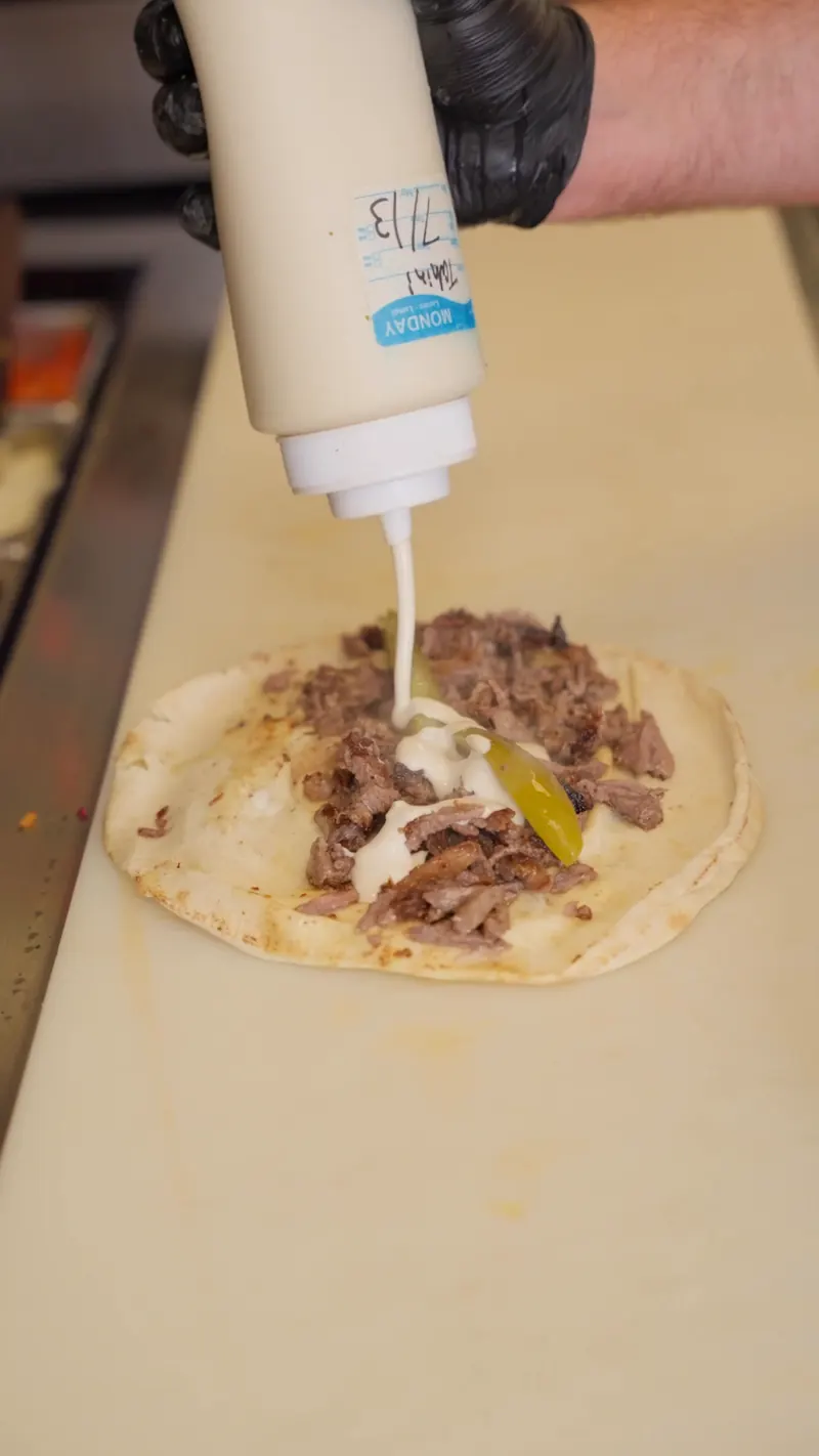 Garlic sauce squeezed over beef shawarma and pickles on an open pita