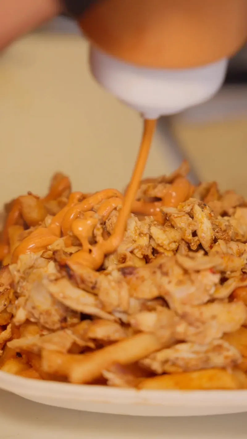 Habibi sauce drizzled over chicken shawarma and fries at the prep counter