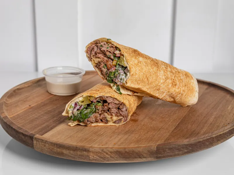 A beef shawarma wrap cut in half on a wooden board