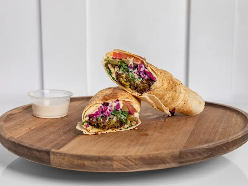 A falafel wrap cut in half on a wooden board