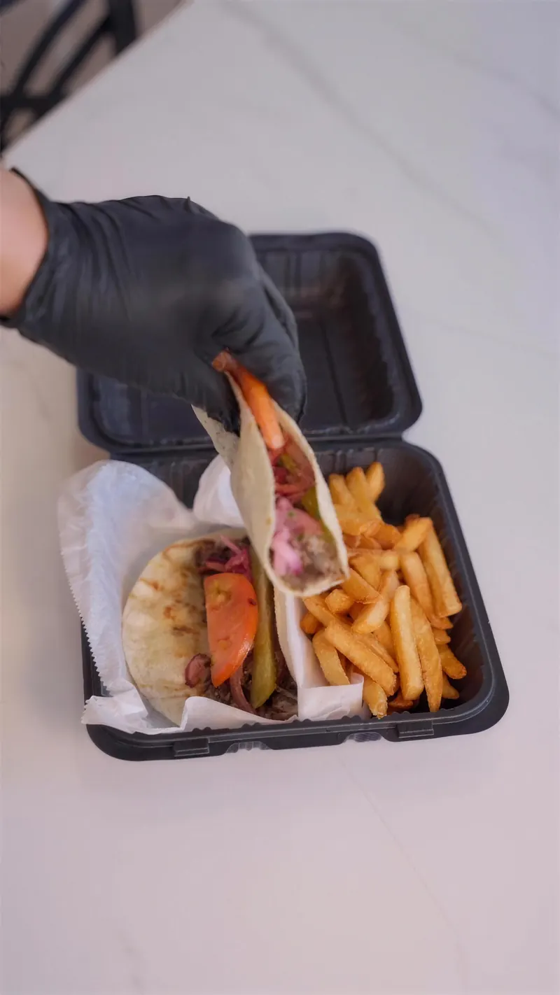 Lifting a shawarma taco out of a to-go box of fries