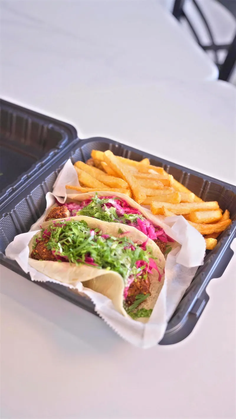 Two spicy falafel tacos and fries in a to-go box
