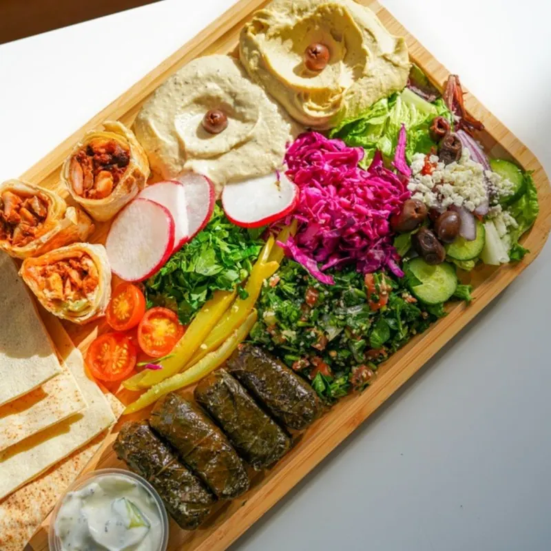 A mezze board with hummus, shawarma bites, grape leaves, tabbouleh, pickled vegetables, feta salad and pita