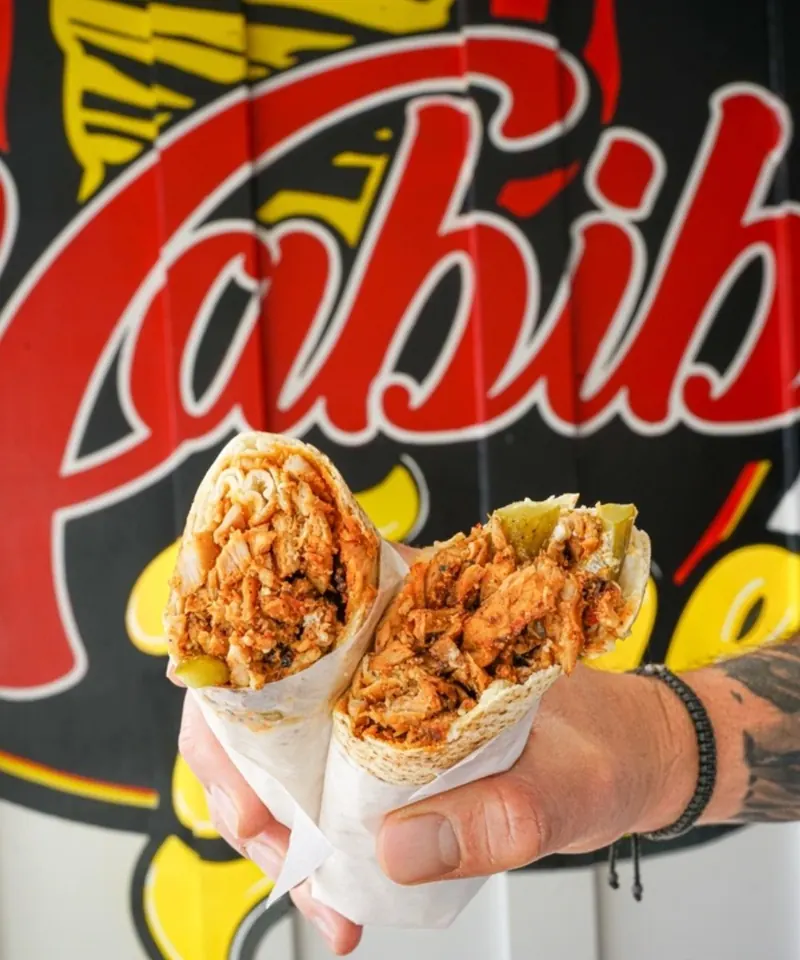 A chicken shawarma wrap held up in front of the Habibi Time mural