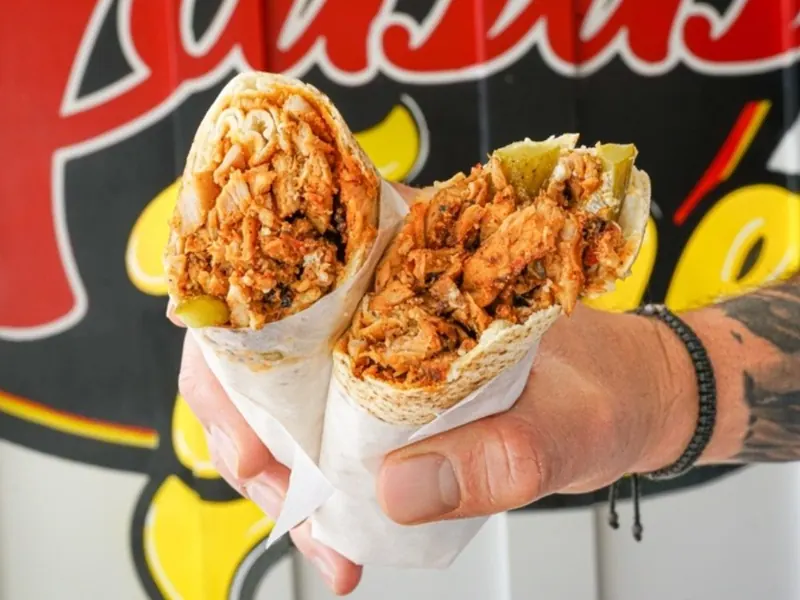 A chicken shawarma wrap held up in front of the Habibi Time mural